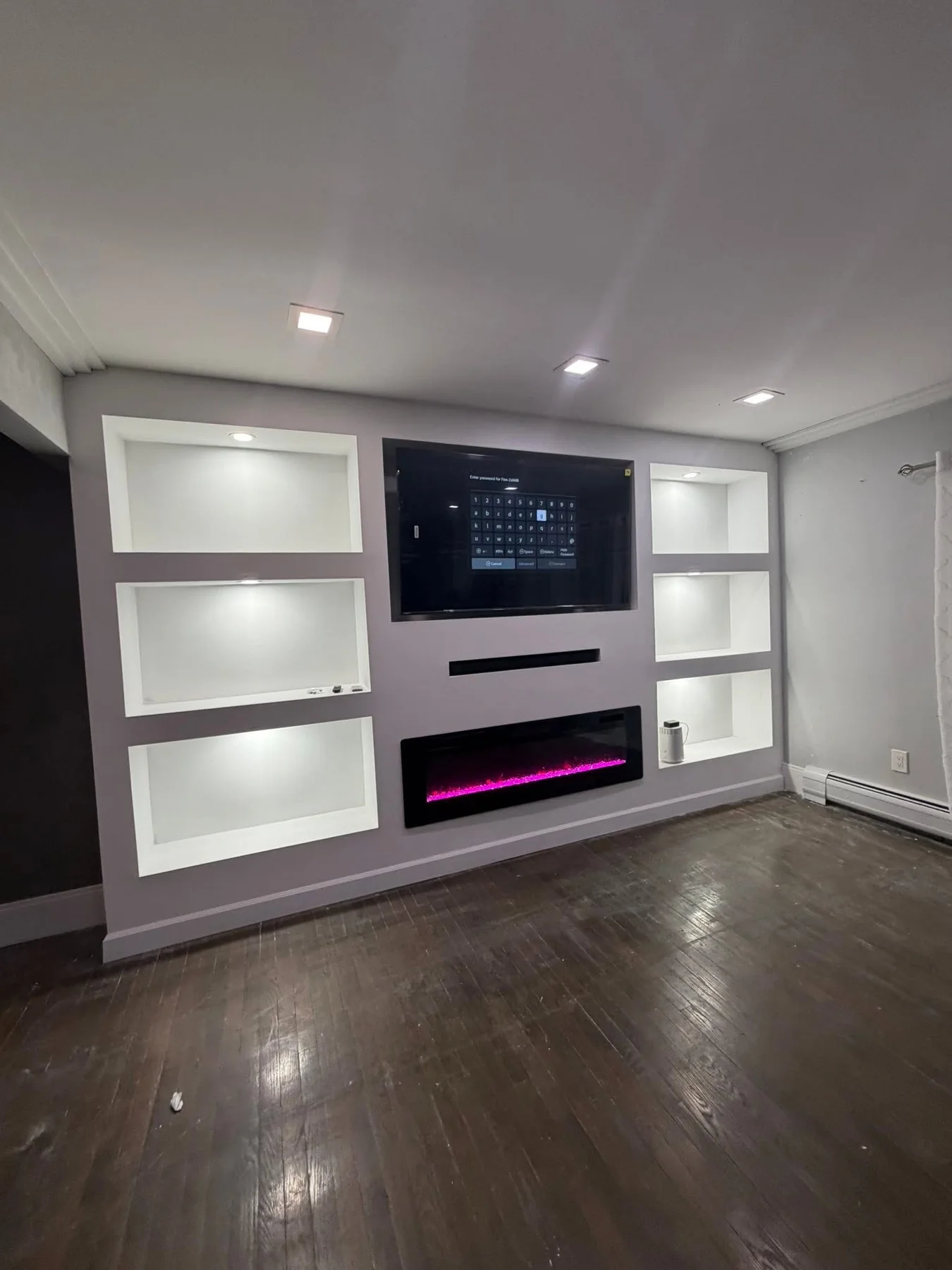 Custom built-in media feature wall with illuminated display shelves, a television, and an electric fireplace